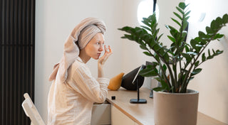 Woman applying lash lift treatment at her vanity after a shower, demonstrating an at-home eyelash lifting routine for natural and enhanced lashes
