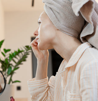 Side view of a woman applying a lash lift treatment in a bathroom, showing the precise technique for lifting and curling natural eyelashes at home